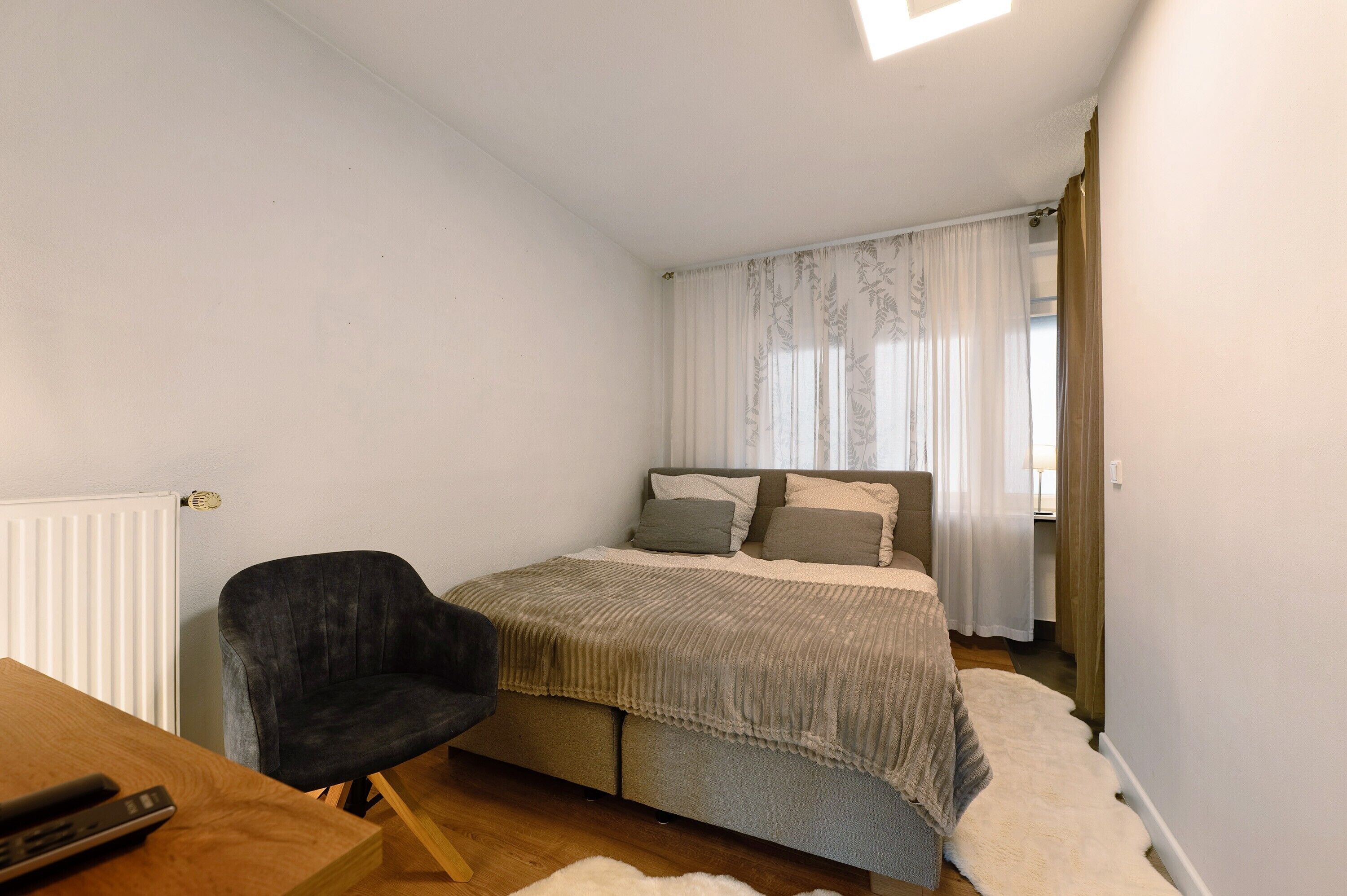 Ein Schlafzimmer mit Bett, Stuhl, Heizkörper und einem Fenster mit Vorhängen.