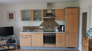 A kitchen with wooden cabinets, a tiled backsplash, a built-in oven, and a television on a stand.