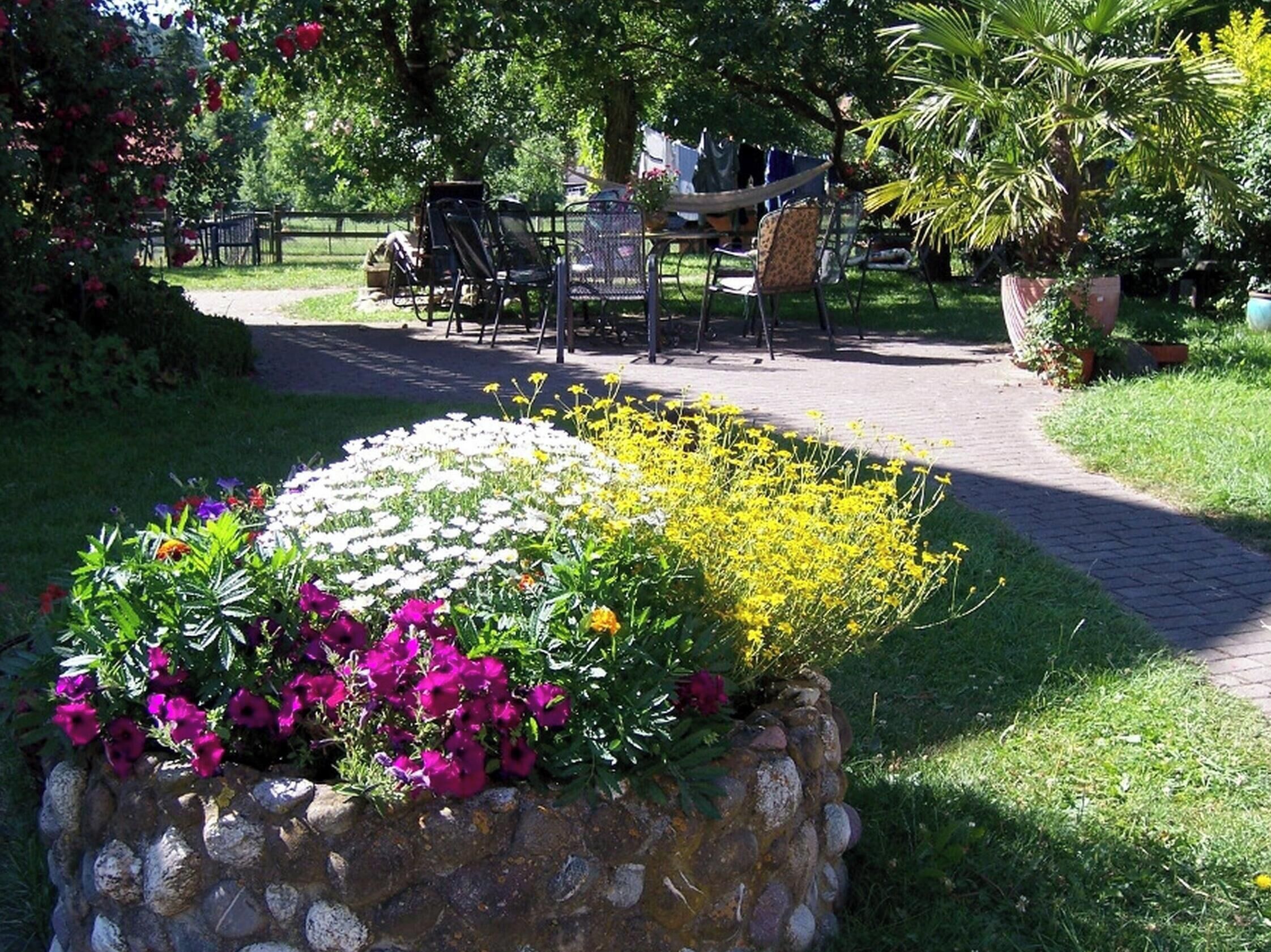Ein Garten mit einem Steinpflanzbeet, einem gepflasterten Weg und Gartenmöbeln.