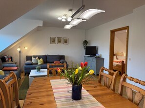 Una sala de estar acogedora con una mesa de comedor de madera, un sofá, un televisor y una estantería.