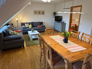 Una sala de estar con sofá, mesa de comedor, sillas, televisor y aparador.