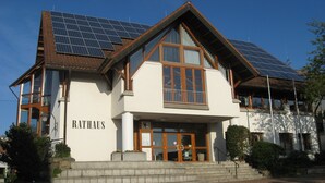 Un edificio con un llamativo letrero 'RATHAUS', amplias ventanas y paneles solares en el techo.