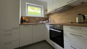 Una cocina moderna con armarios blancos, encimera de madera, horno empotrado y ventana con vistas a zonas verdes.