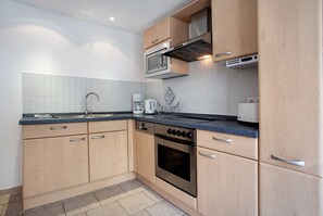 A modern kitchen with wooden cabinets, a stainless steel oven, a microwave, and a coffee maker.