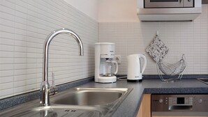 A kitchen with a stainless steel sink, a coffee maker, a kettle, and a microwave.