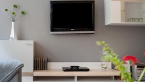 A modern living room with a flat-screen TV mounted on the wall, a wooden console table with books and a remote, and a vase with flowers.