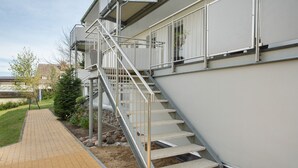 A staircase leading to a building with a metal railing, a paved walkway, and a small garden area with rocks and plants.