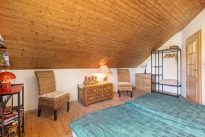 A cozy attic bedroom with wooden ceiling, a bed, two wicker chairs, a dresser, and a bookshelf. - Apartment 'An Der Bieke' with Shared Terrace, Shared Garden and Wi-Fi (Olsberg)