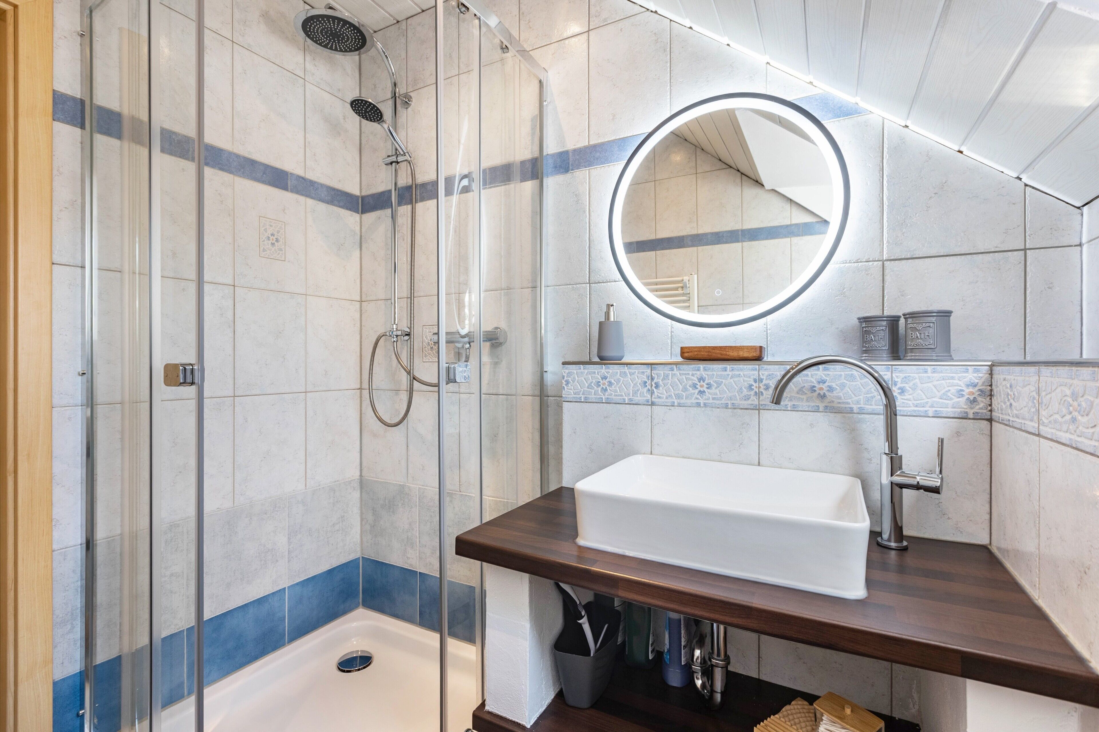 A bathroom with a glass-enclosed shower, a white sink, and a mirror with a circular frame.