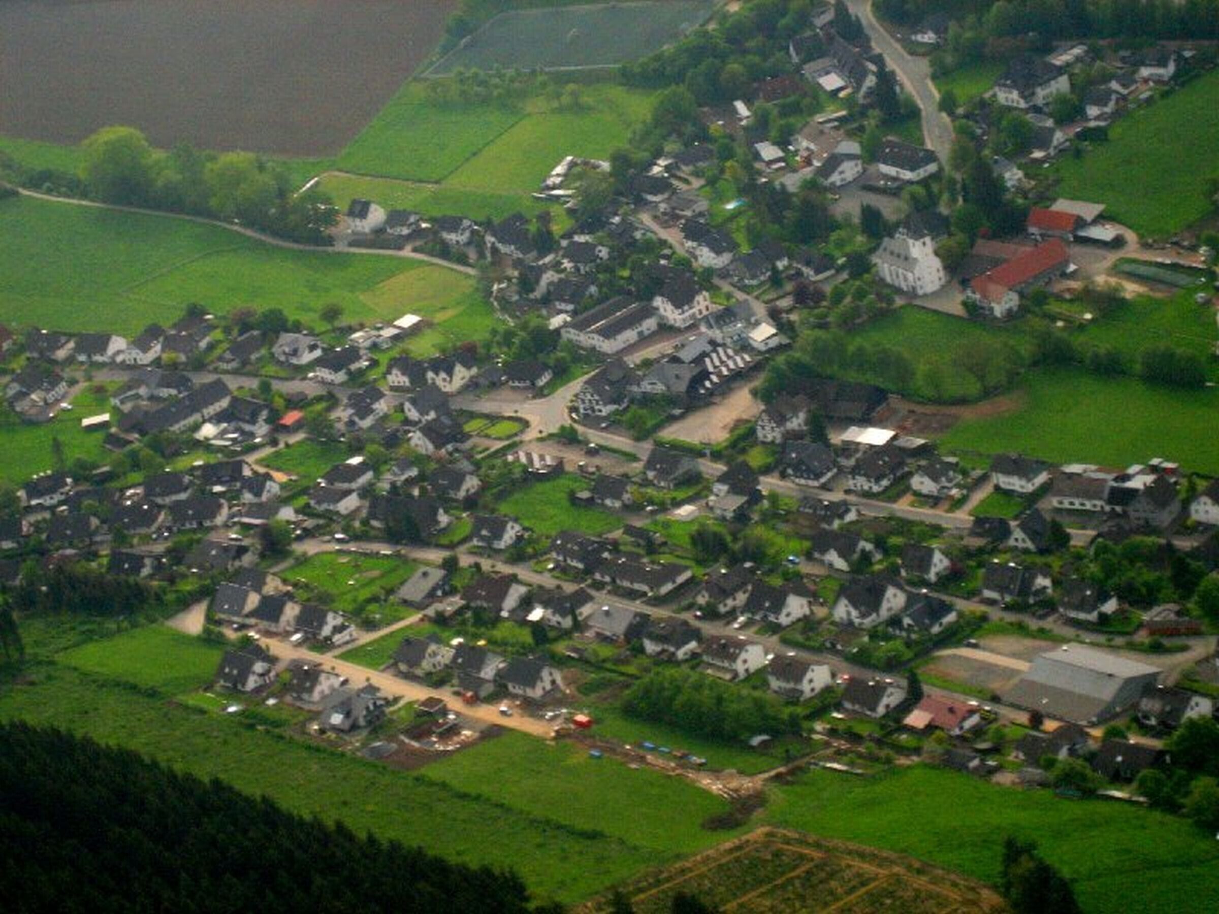 Luchtbeeld van een dorp met huizen, wegen en groene velden.