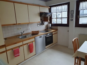 Una cucina con mobili in legno, lavastoviglie, piano cottura e una finestra con tende di pizzo.