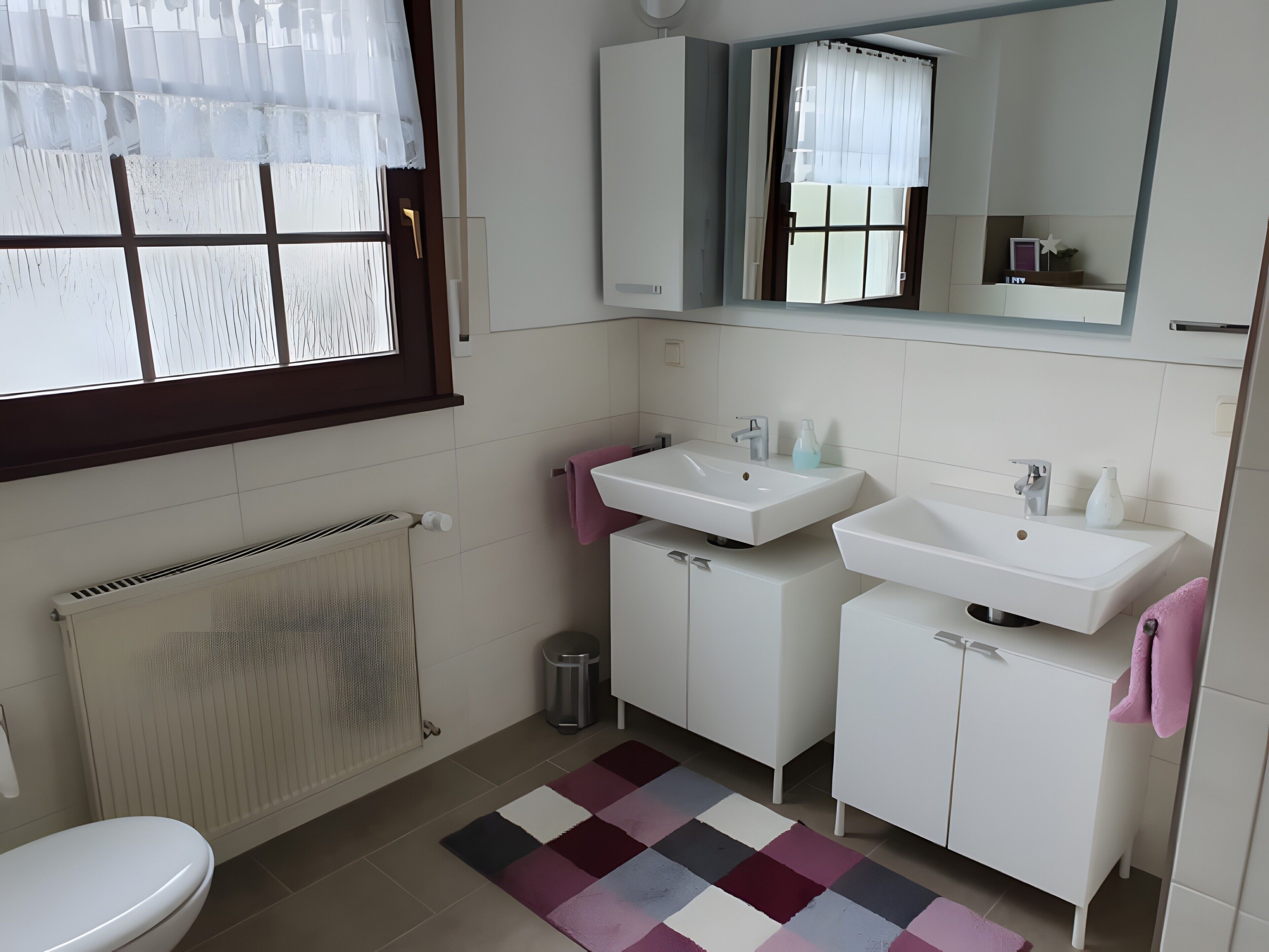 A bathroom with a toilet, two sinks, a mirror, and a radiator.