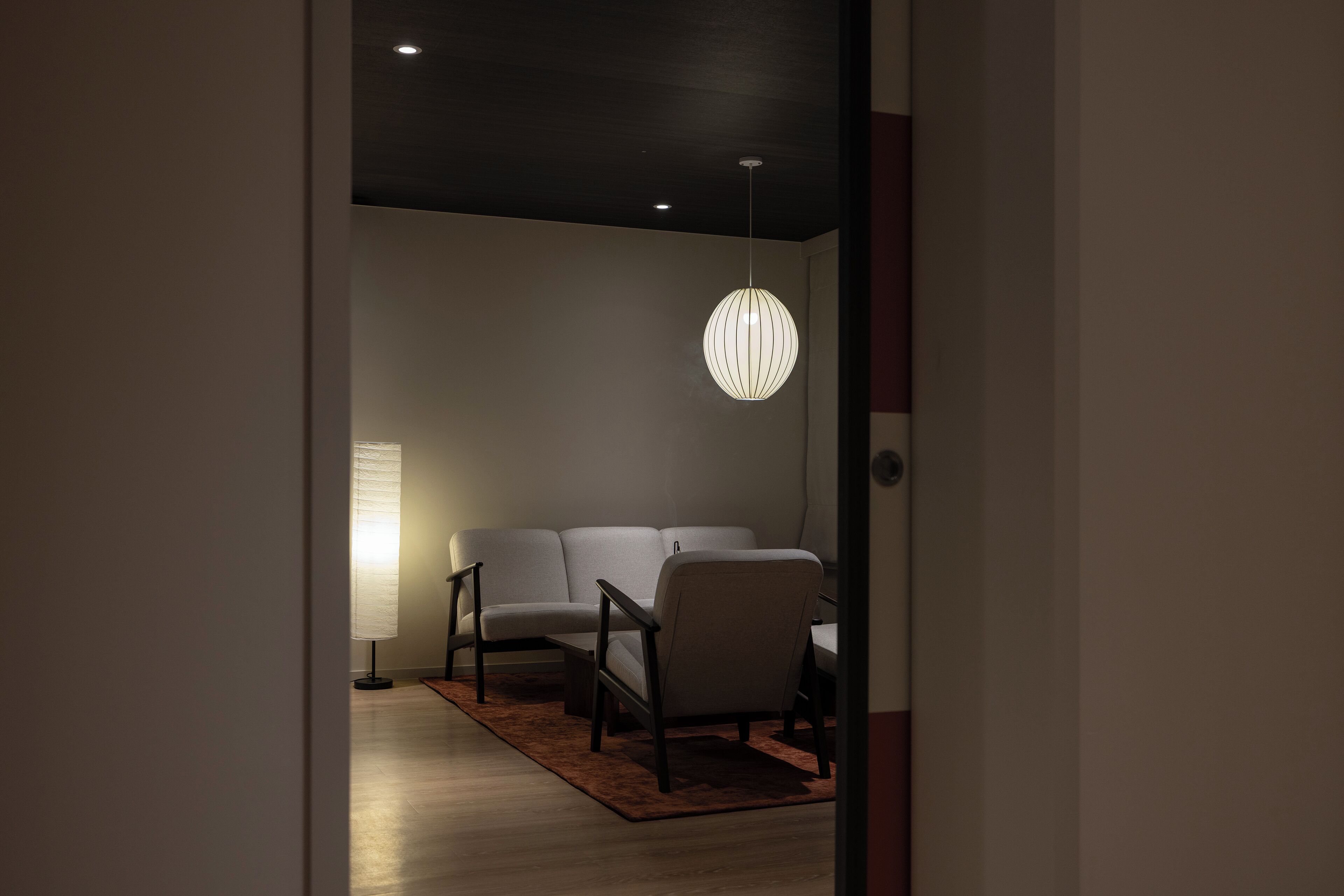 A modern living room with a sofa, armchairs, and a hanging light fixture.