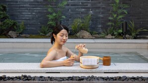 A person sitting by a pool with a wooden bowl and a cup, surrounded by plants and a brick wall. - Koum Ryokan Hotel Gijang by Anook (Busan)