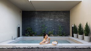 A person in a modern outdoor pool with a black brick wall, potted plants, and a wooden lounge chair. - Koum Ryokan Hotel Gijang by Anook (Busan)