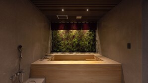 A modern bathroom with a wooden bathtub, a shower area, and a wall with a vertical garden. - Koum Ryokan Hotel Gijang by Anook (Busan)