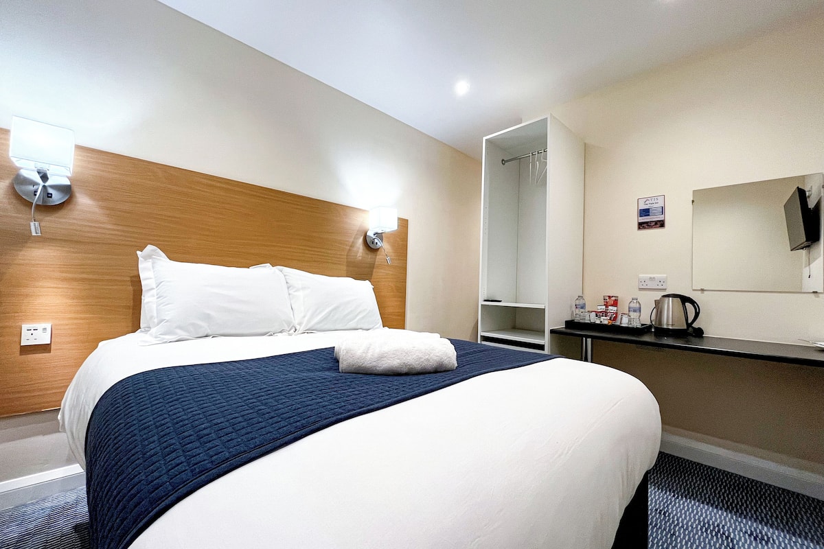Habitación de hotel con cama, mesita de noche con lámpara, espejo y armario.