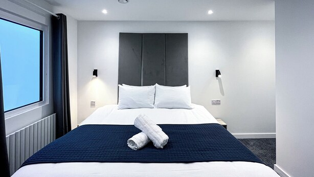 A modern hotel room with a large bed, a dark blue quilted bedspread, white pillows, and a neatly folded towel on the bed. - Park Inn Palace (Dover)