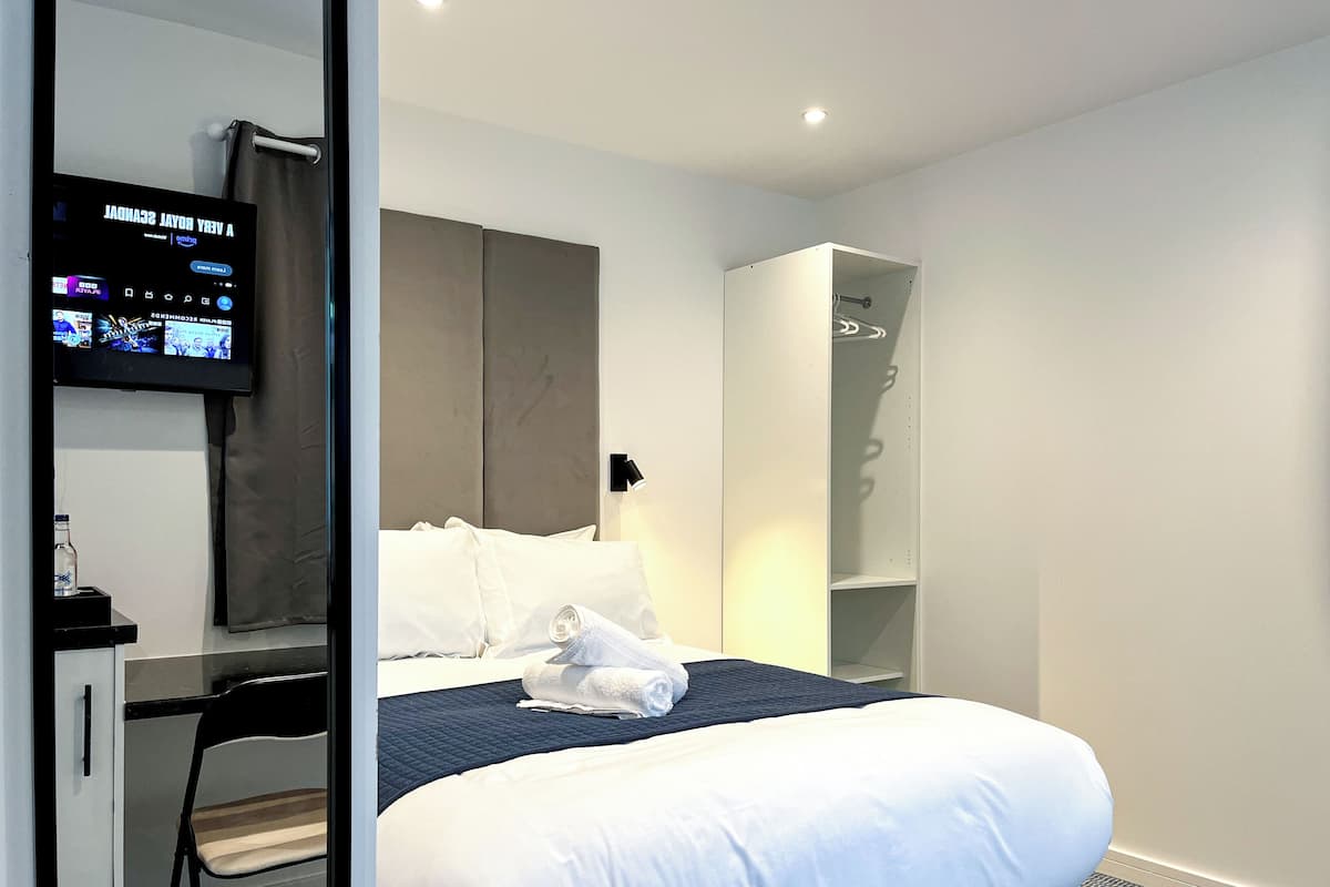 Una habitación de hotel con cama, escritorio, silla, televisión y armario.