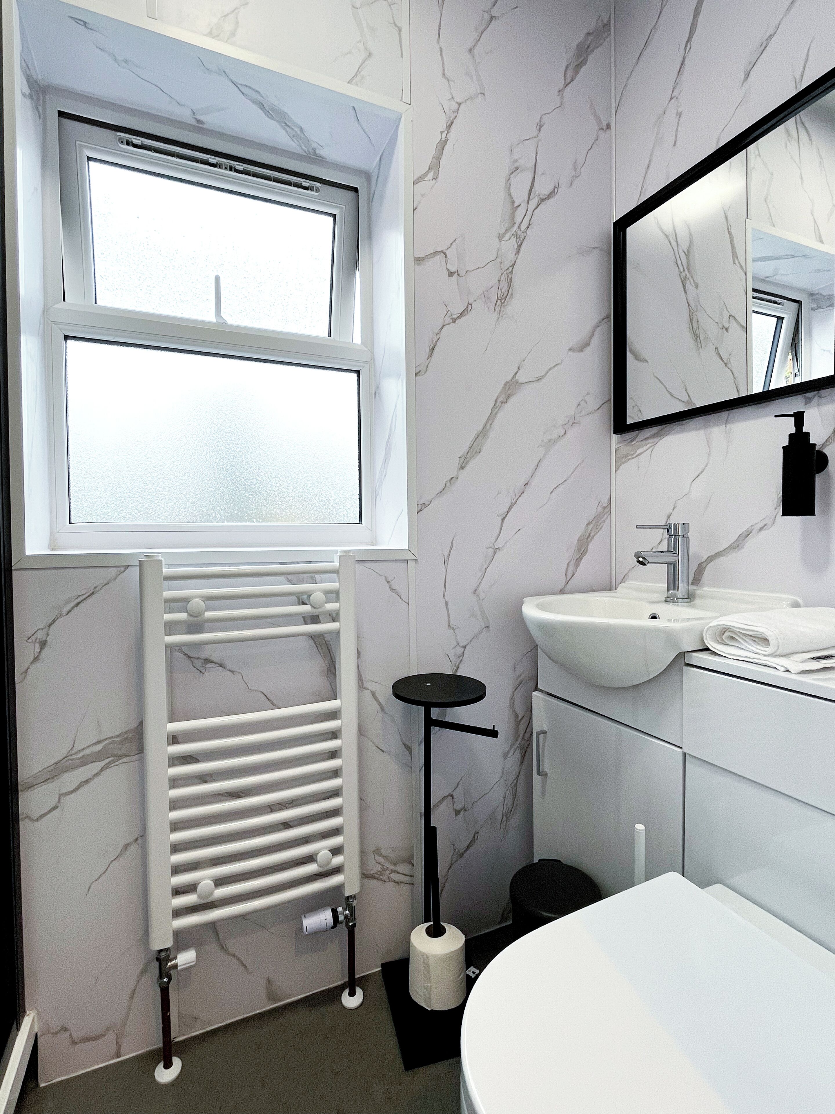A modern bathroom with a white vanity, a large mirror, a toilet, and a radiator.