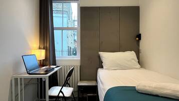 Ein Hotelzimmer mit einem Bett, einem Schreibtisch mit einem Laptop, einem Stuhl und einem Fenster mit Blick auf Gebäude.