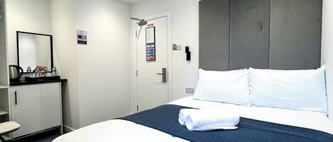 Habitació d'hotel amb un llit, una taula de nit, un mirall i una porta.