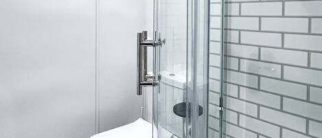 Un baño moderno con cabina de ducha de vidrio, inodoro blanco y pared con azulejos.