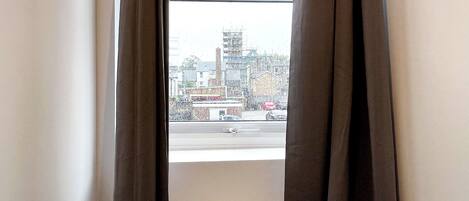 A window with brown curtains, a view of a cityscape with buildings and a road.