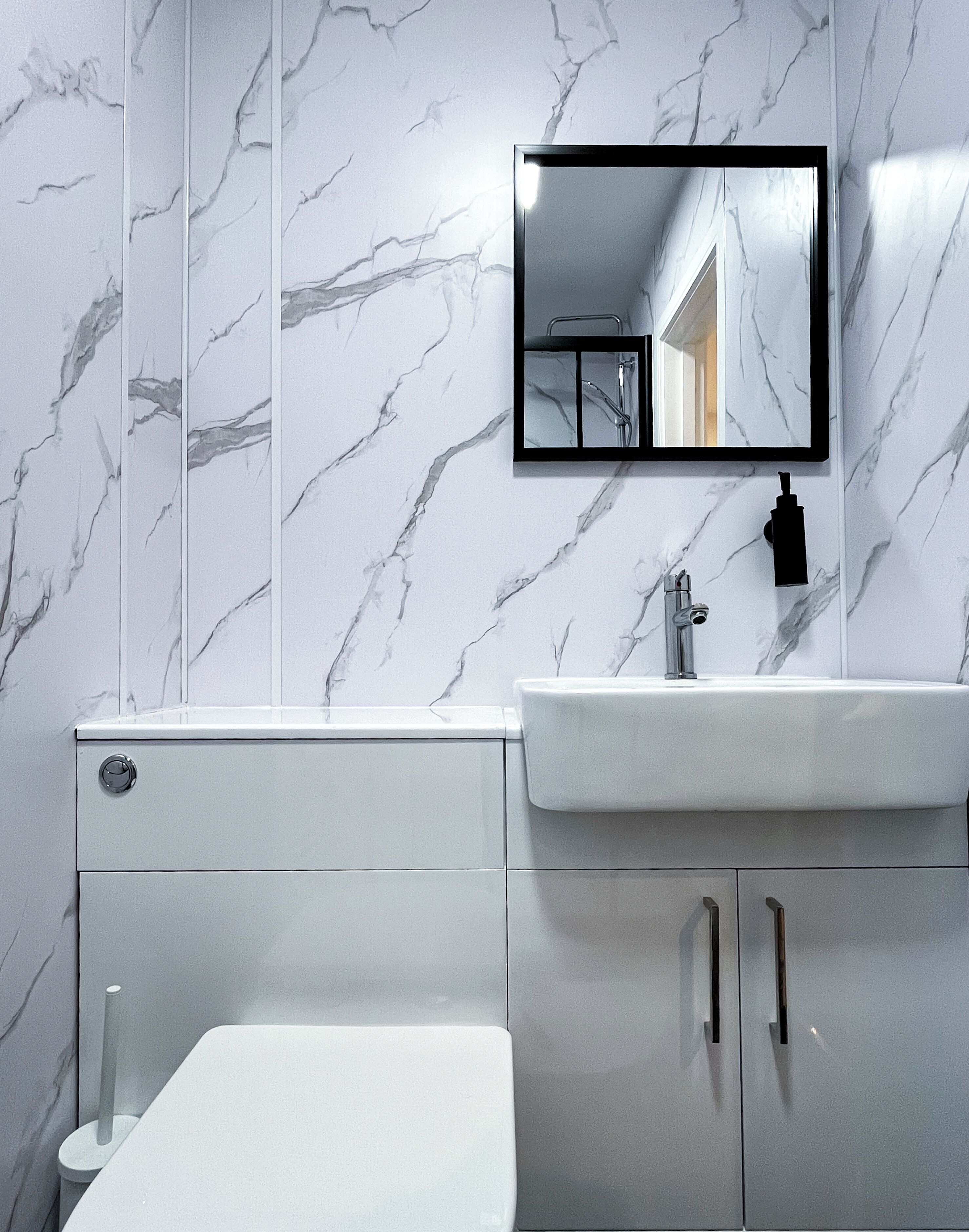 A bathroom with a white marble wall, a white sink, a mirror, and a toilet.
