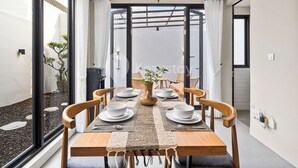 Comedor con mesa de madera dispuesta para cuatro personas, sillas alrededor y vista a un jardín a través de grandes ventanales.