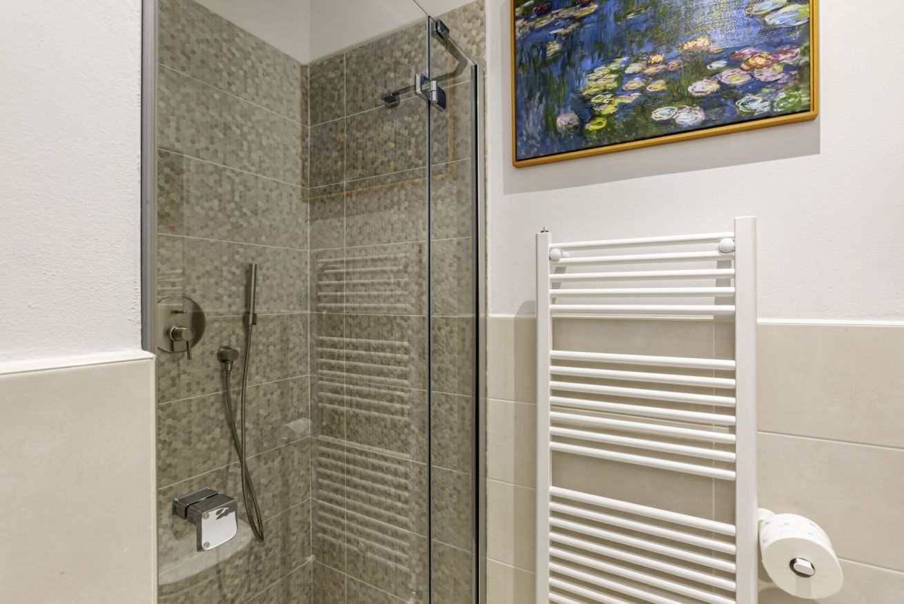 A shower with a glass door, a white towel rack, and a painting of water lilies on the wall.