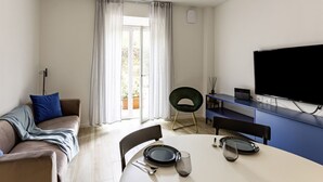 Un salon moderne comprenant un canapé, une table à manger, des chaises, un téléviseur à écran plat et une grande fenêtre avec des rideaux.