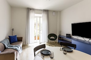 Un salon moderne comprenant un canapé, une table à manger, des chaises, un téléviseur à écran plat et une grande fenêtre avec des rideaux.