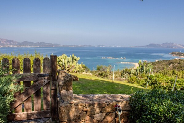 A coastal landscape with a wooden gate, a stone wall, and a view of the sea.