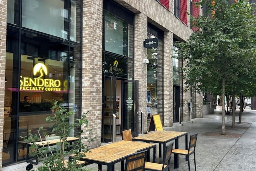 Tiilestä rakennettu liikerakennus, jonka edessä on kyltti, jossa lukee ”Sendero Specialty Coffee”. Sisäänkäynnin edessä on ulkokalusteita, kuten pöytiä ja tuoleja.