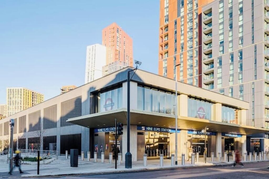 A modern building with a glass facade, signage for 'Nine Elms Station', and a pedestrian entrance.