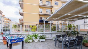 Zona de pati exterior amb taula de futbolí, taula de dinar amb cadires i plantes en testos.