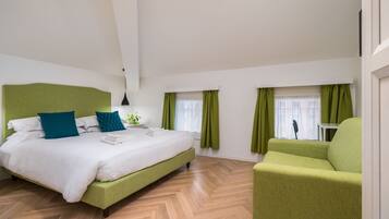 A modern hotel room with a large bed, green upholstered armchair, and a view of the city through the windows.