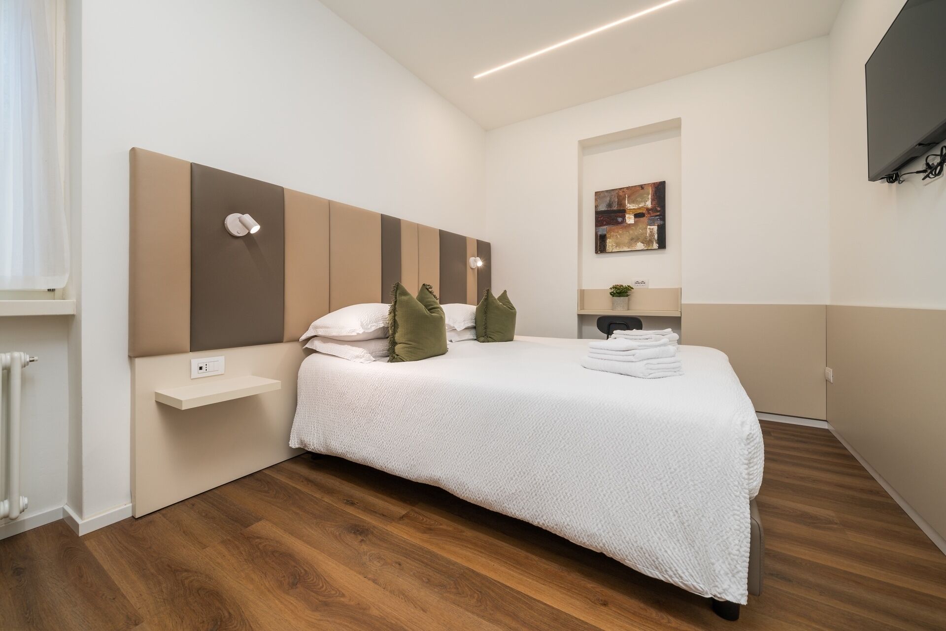 Ein modernes Schlafzimmer mit einem großen Bett, einer Kopfteilbeleuchtung, einem Nachttisch und einer kleinen Arbeitsfläche.