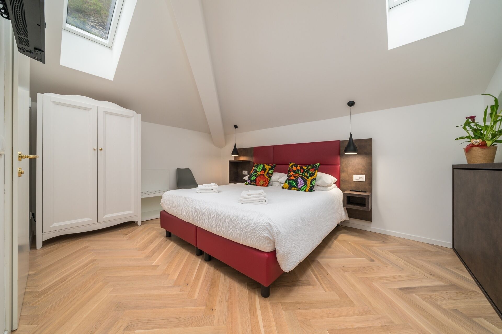 Ein modernes Schlafzimmer mit einem großen Bett, einem Kleiderschrank, einem Schreibtisch und einer Topfpflanze.