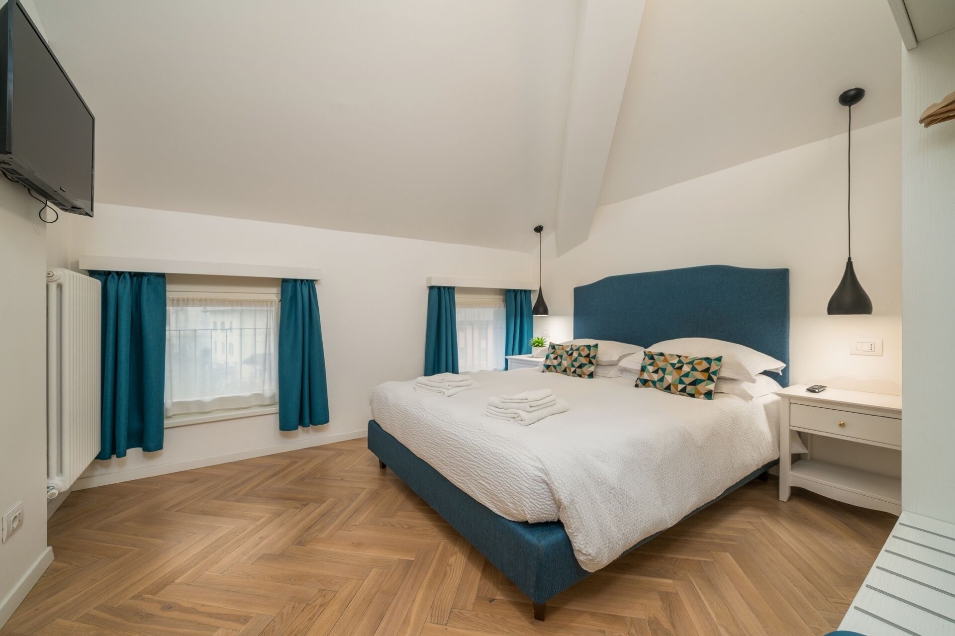 Um quarto moderno com uma cama grande, uma mesa de cabeceira, uma escrivaninha e uma TV fixada na parede.
