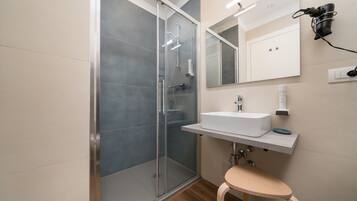 Une salle de bain moderne avec une douche à parois de verre, un lavabo blanc et un tabouret en bois.