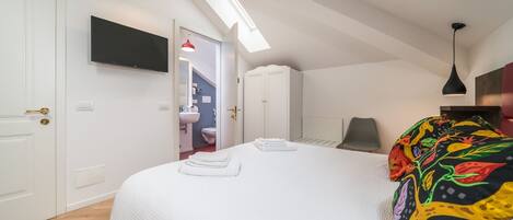 A bedroom with a large bed, a TV mounted on the wall, a skylight, and a wardrobe.