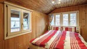 A wooden cabin bedroom with a bed, two windows, and a ceiling fan. - StayBrienz - Lake Brienz Holiday Apartment (Brienz)