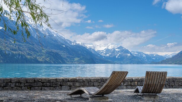 Two wooden lounge chairs on a stone wall by a lake with mountains in the background. - StayBrienz - Lake Brienz Holiday Apartment (Brienz)