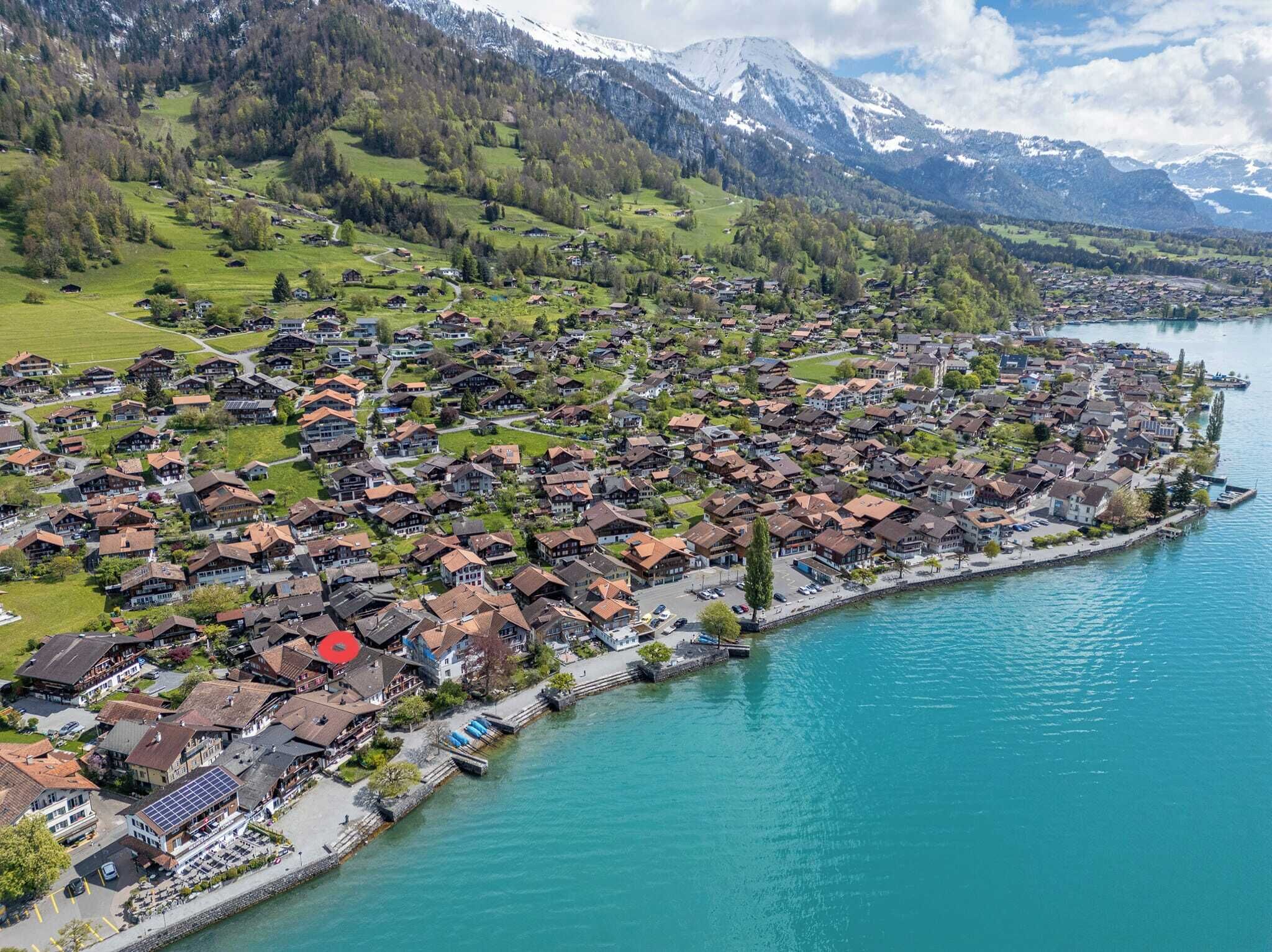A lakeside village with traditional houses, a marina, and a backdrop of mountains.