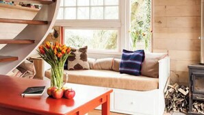 Una habitación acogedora con detalles de madera, un banco empotrado con cojines, una mesa con un jarrón de flores y una chimenea.