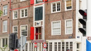 Un edificio de varios pisos con contraventanas rojas, un letrero de café a la vista y un semáforo.