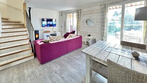 Una sala de estar con una escalera, un televisor de pantalla plana, un sofá y una mesa de comedor.