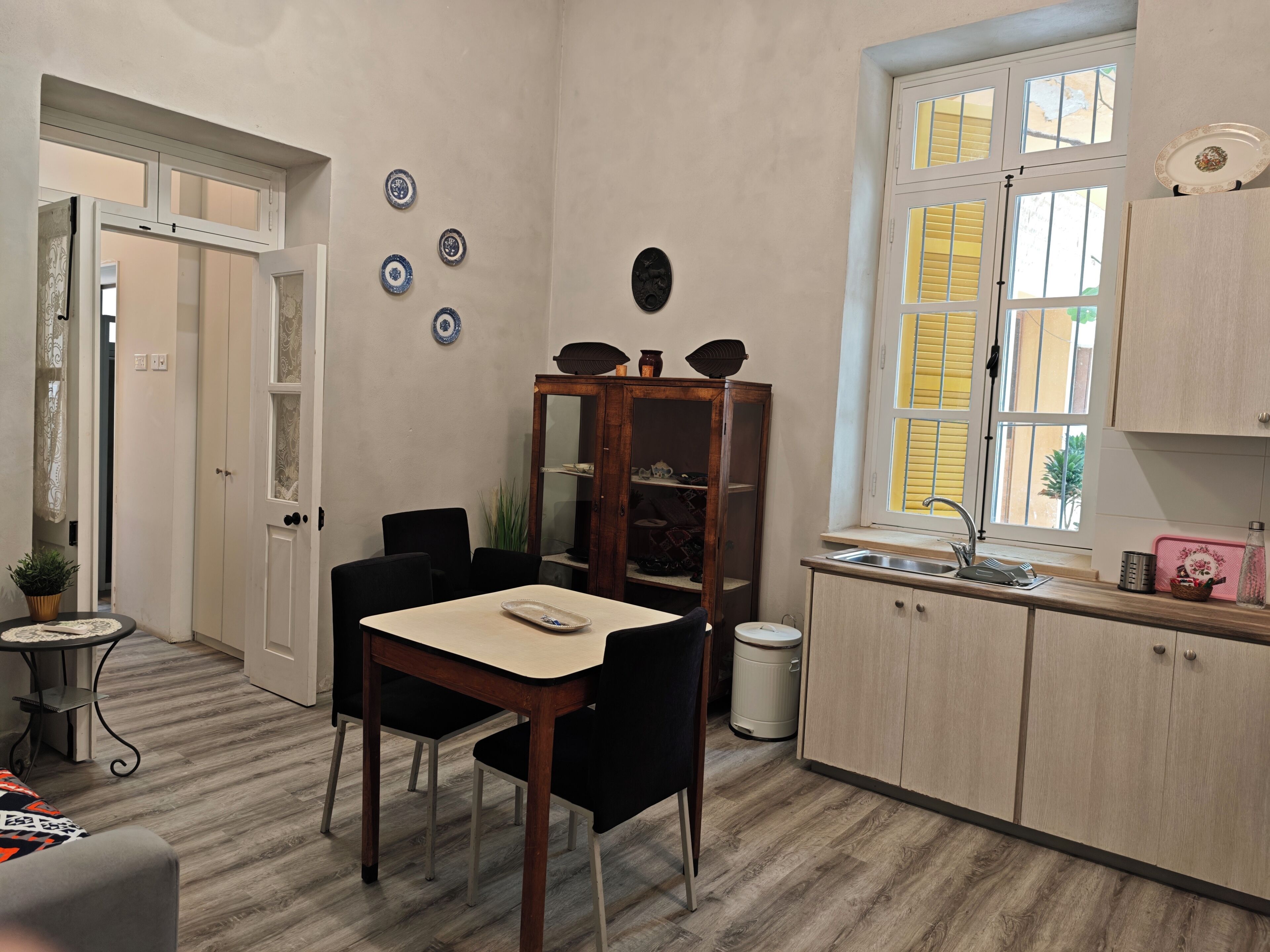 A compact kitchen with a dining table, chairs, a cabinet, and a window with yellow shutters.